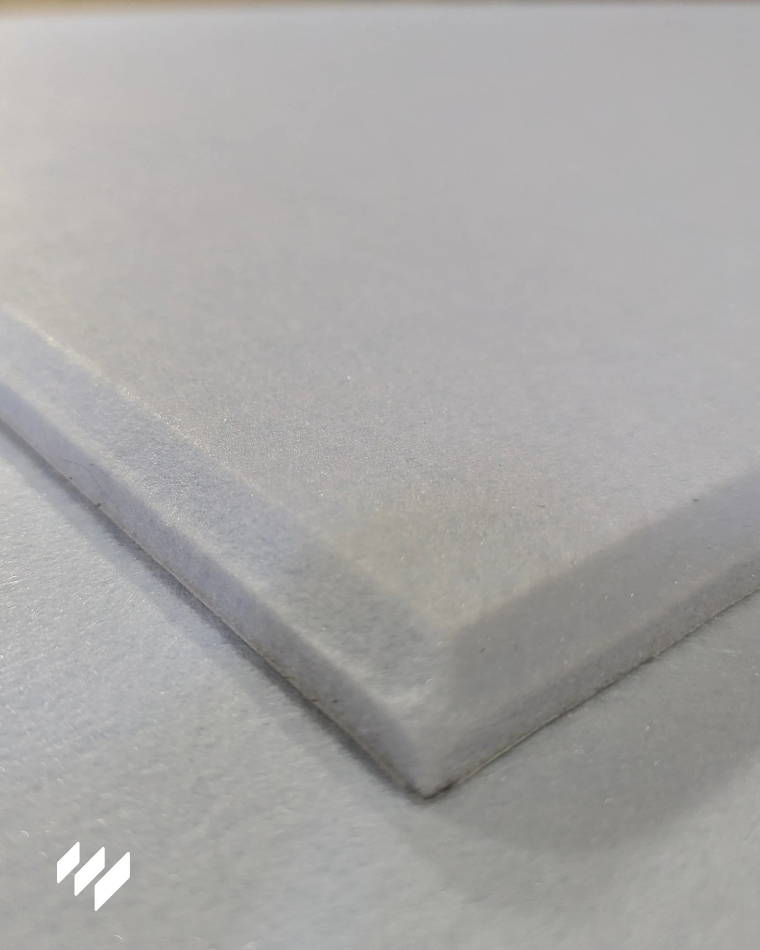 Detalle en primer plano del borde de la espuma acústica blanca de poliéster, mostrando textura suave y acabado de alta calidad.