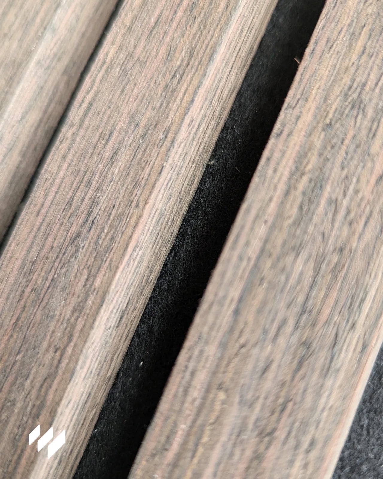 Detalle en primer plano del acabado en madera Roble Ahumado del panel acústico autoadhesivo de listones 3D, mostrando la textura realista y el fieltro negro PET entre los listones.