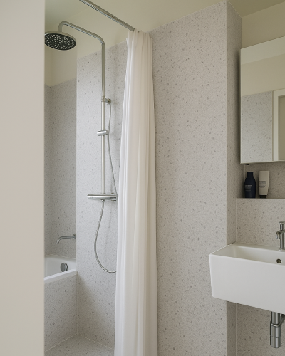 Espacio de ducha con paredes revestidas con panel SPC efecto terrazo, columna de ducha moderna y cortina blanca, junto a un lavabo suspendido.