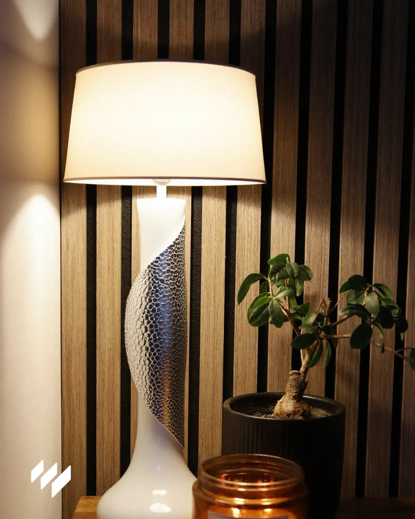 Panel acústico de listones Nogal Natural de Revestimientos Pared en un rincón decorado con lámpara moderna, planta y vela aromática, ideal para ambientes con luz cálida y texturas naturales.