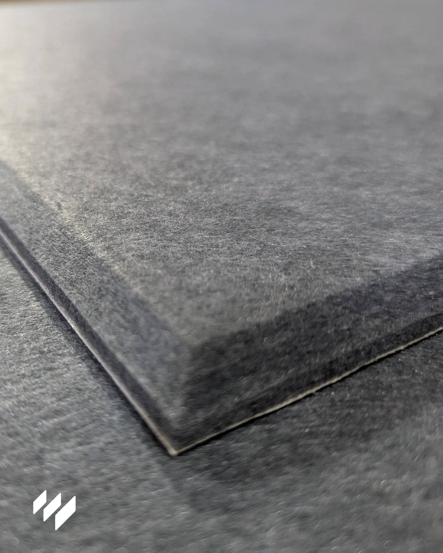 Primer plano del borde del panel insonorizante autoadhesivo de poliéster gris, mostrando su textura suave y densidad del material.
