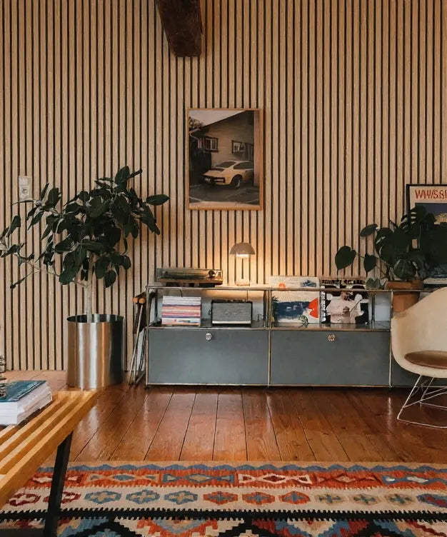 Revestimiento de pared con listones acústicos en color roble natural, decorado con plantas, alfombra bohemia y muebles metálicos vintage.