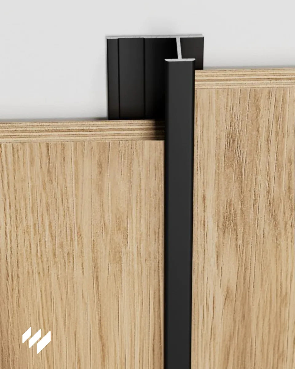Perfil de unión en H de aluminio negro mate instalado entre dos paneles decorativos de revestimientos pared, mostrando el acabado limpio y la unión vertical.