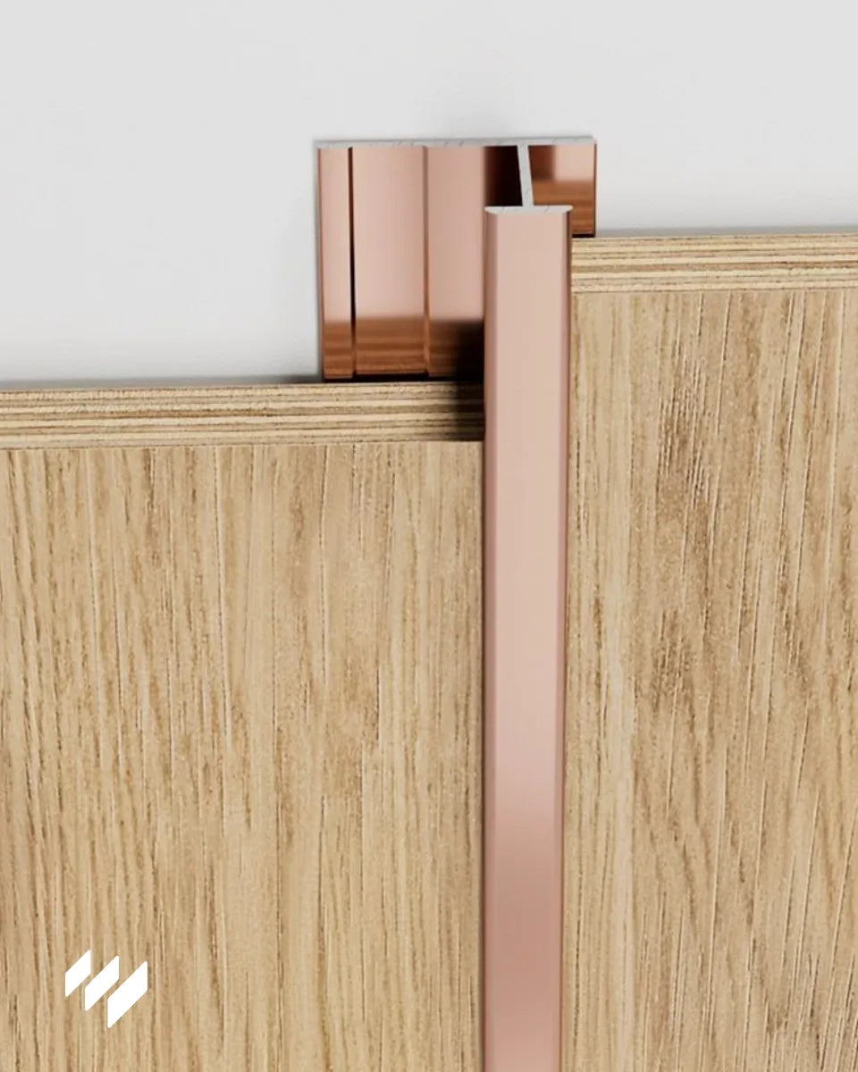 Perfil de unión en H de aluminio en acabado oro rosa brillante instalado entre dos paneles decorativos de revestimientos pared, mostrando la unión vertical y el acabado pulido.