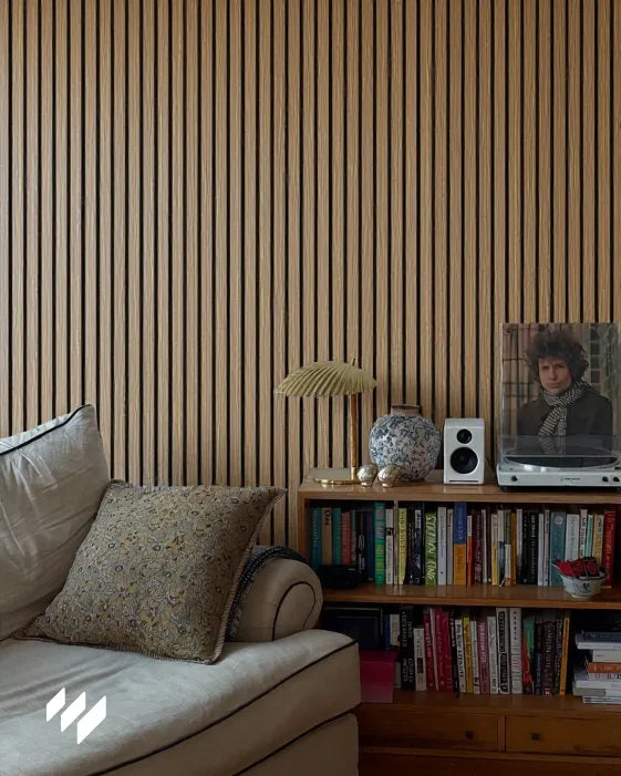 Zona de lectura acogedora con pared de listones acústicos en roble natural de revestimientos pared, estantería de libros y tocadiscos decorativo.