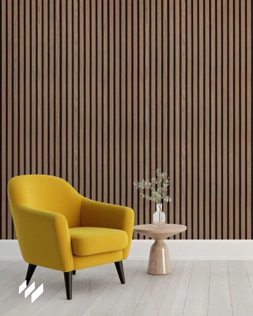 Panel acústico de listones Nogal Natural de Revestimientos Pared instalado en una sala luminosa con un sillón amarillo mostaza y mesa auxiliar, creando un ambiente acogedor y elegante.