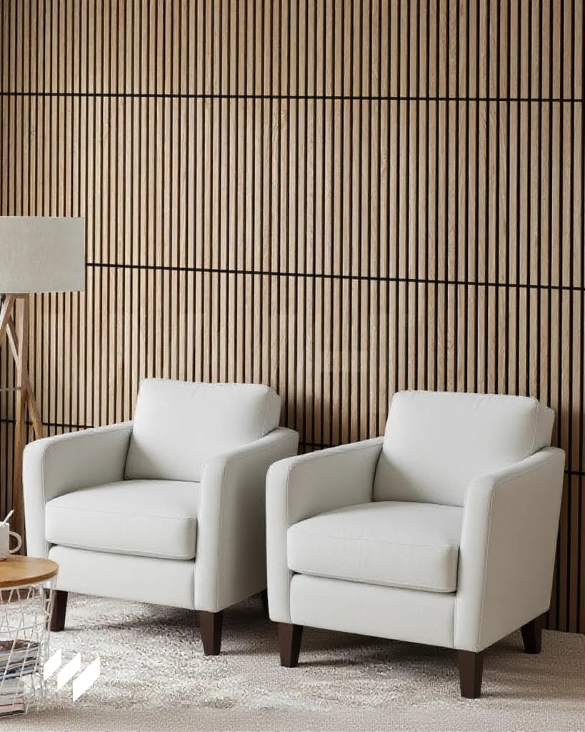 Dos sillones blancos frente a una pared revestida con paneles acústicos autoadhesivos de listones en color roble natural, creando un ambiente cálido y moderno en el salón.