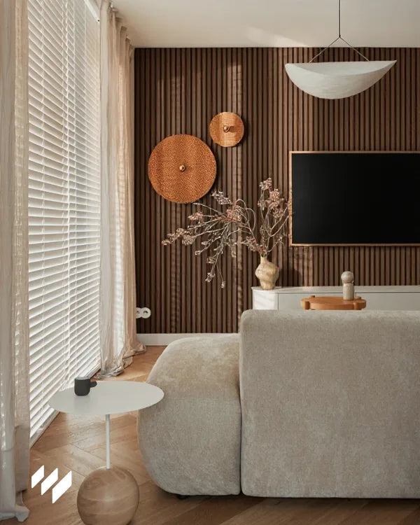 Revestimientos Pared presenta su revestimiento en Roble Ahumado instalado detrás del televisor en salón moderno con sofá claro y luz natural filtrada por cortinas.