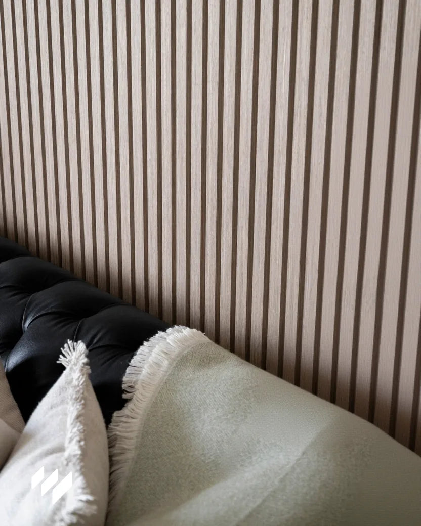 Primer plano del panel acústico de listones en color Nogal Natural instalado por Revestimientos Pared, mostrando la textura y los detalles del acabado en un entorno acogedor. sofá de cuero negro