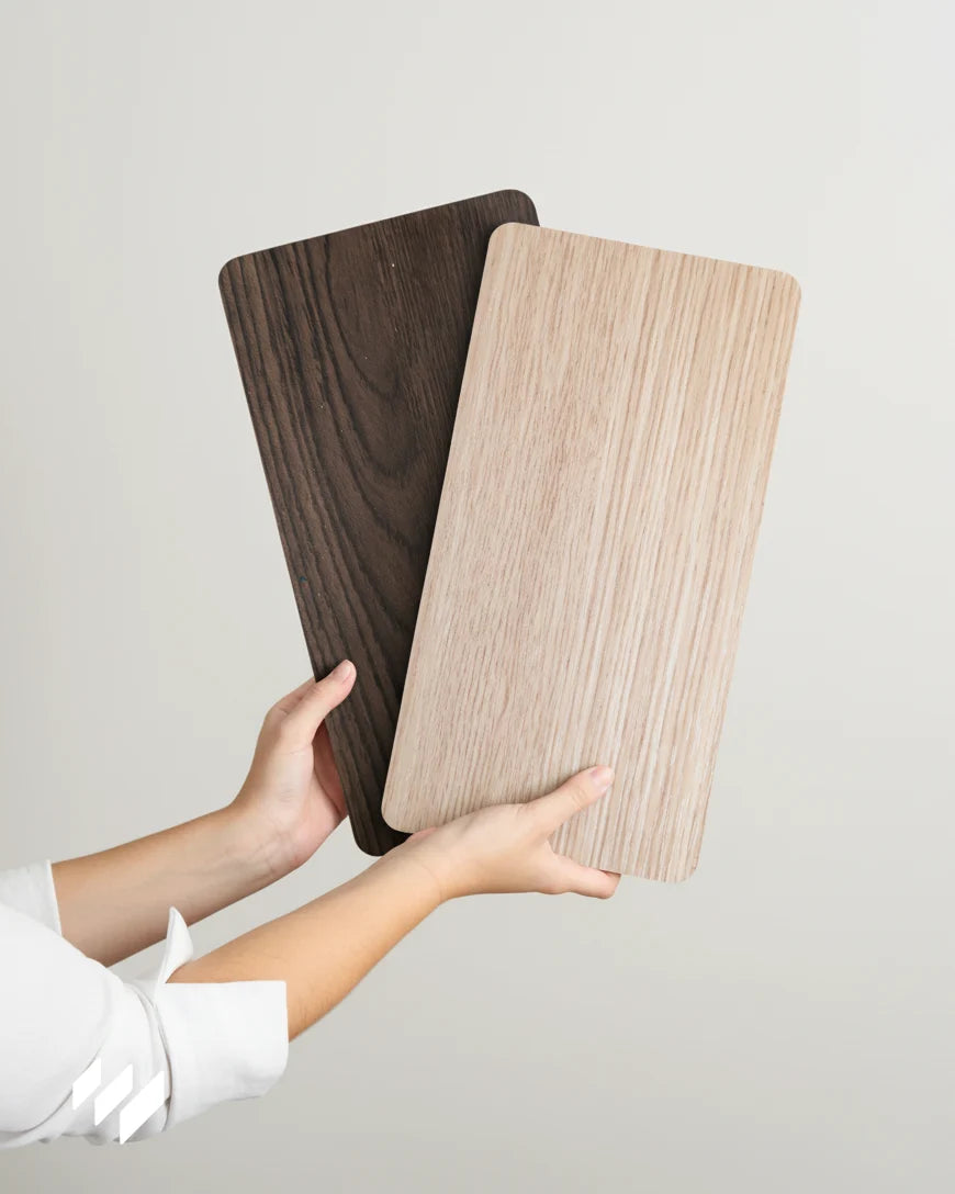 Muestra de la Caja de Muestras Kore con dos paneles WPC efecto madera sostenidos con ambas manos, uno en tono roble natural y otro en roble nocturno — Revestimientos Pared.