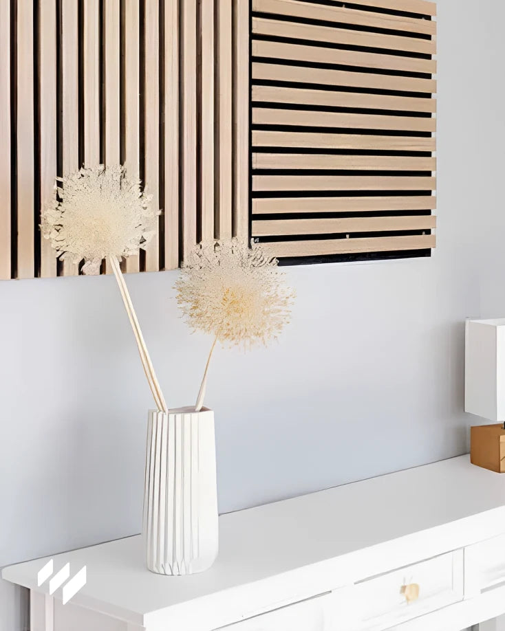 Muestra decorativa de dos tipos de paneles acústicos de listones en color Roble Natural montados en una pared, junto a una consola blanca minimalista.