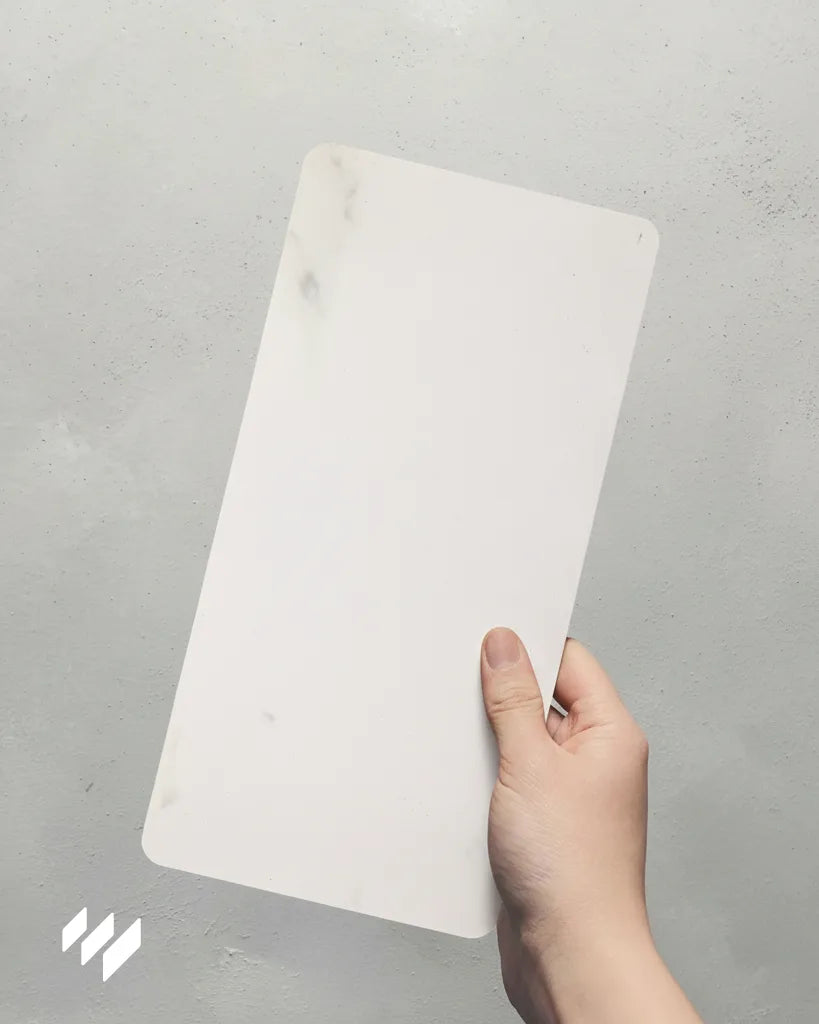 Muestra de panel WPC mate efecto mármol Calacatta Blanco sostenida con una mano, de Revestimientos Pared.