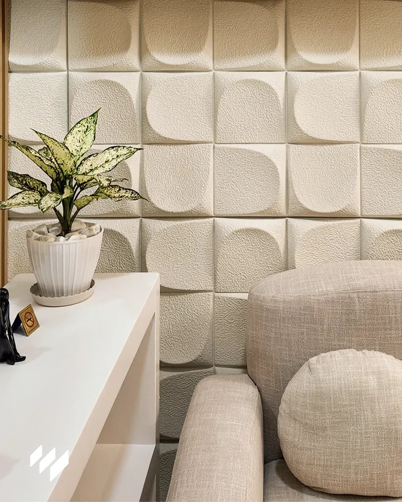 Detalle de pared con Panel decorativo 3D de PU efecto Almohadillado blanco de Revestimientos Pared junto a un sofá beige y mueble auxiliar, ofreciendo ideas para decoración de salón acogedor.