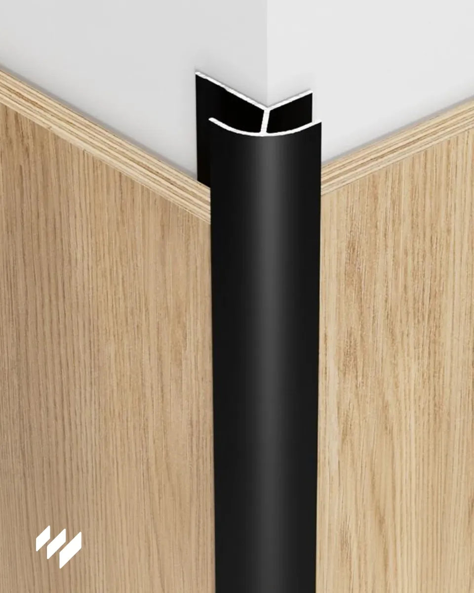 Perfil de esquina exterior redondeada de aluminio negro mate instalado en una esquina con paneles efecto madera.