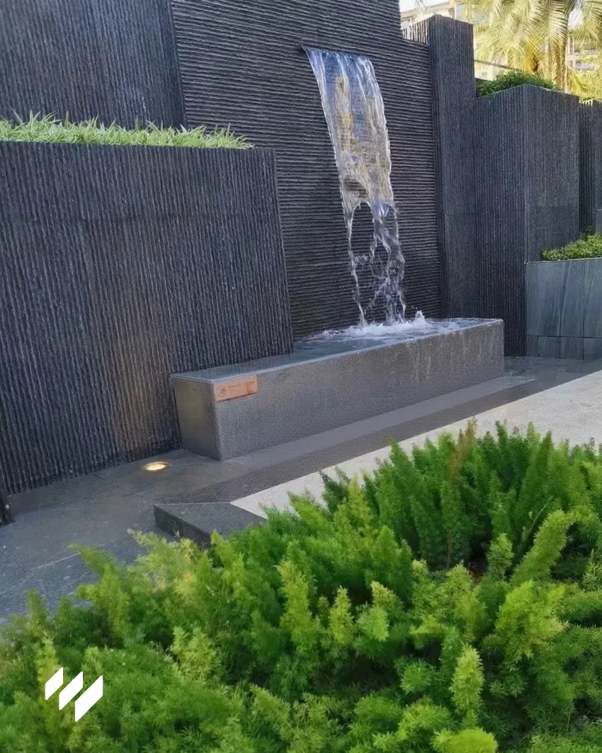Cascada moderna revestida con Revestimiento de pared efecto piedra acanalada negro de Revestimientos Pared, ideal para proyectos de paisajismo y decoración de exteriores.