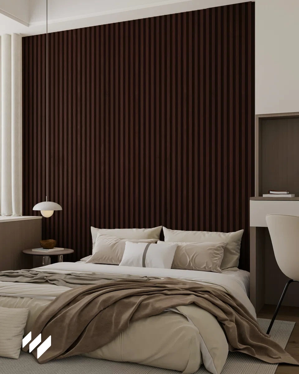 Dormitorio elegante con cabecero revestido con paneles listones 3D WPC Nogal Oscuro de Revestimientos Pared, ropa de cama en tonos beige y lámpara moderna.
