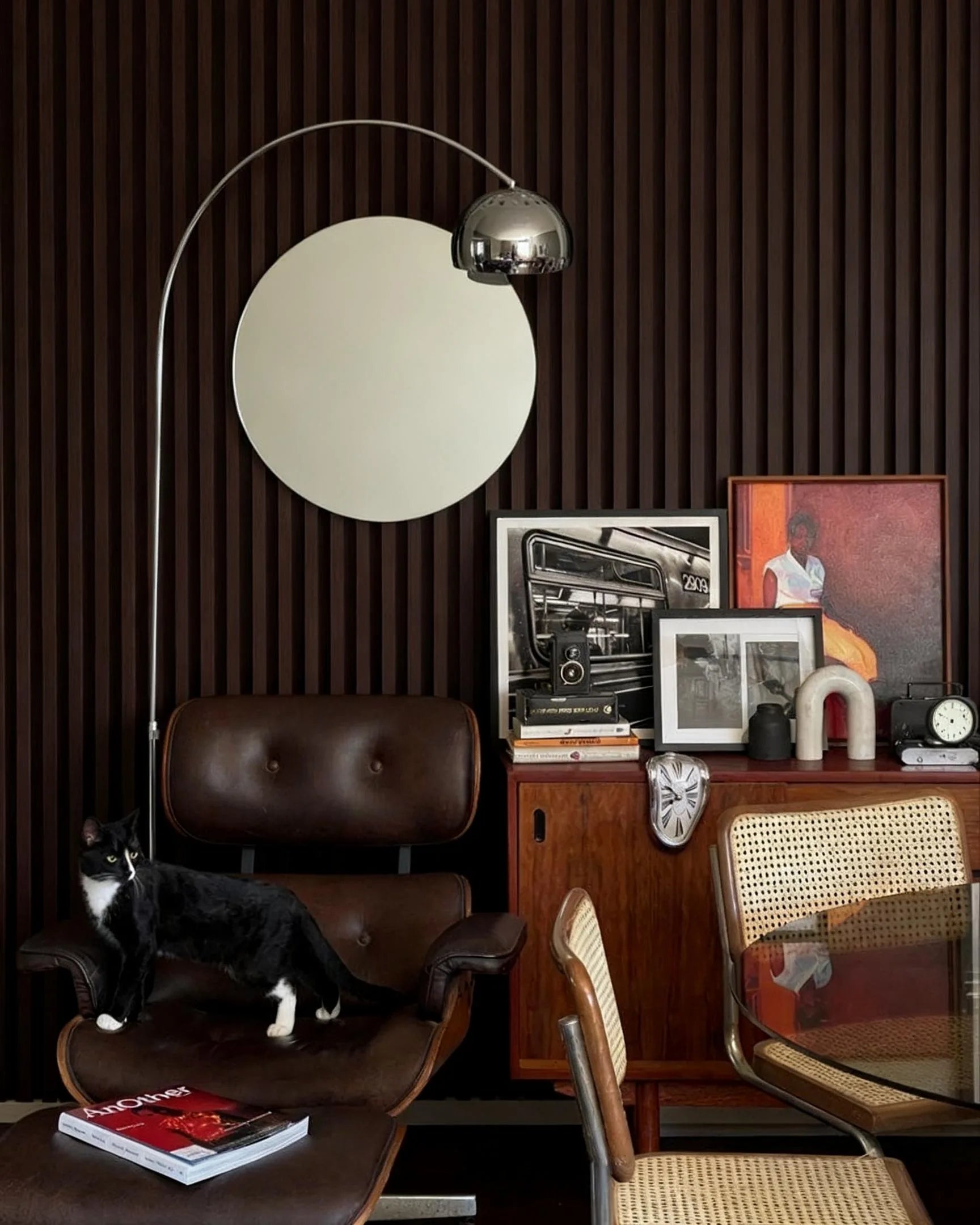 Rincón de lectura con pared revestida en Listones 3D WPC Nogal Oscuro, sillón de cuero marrón y decoración vintage que aporta un estilo sofisticado y acogedor.