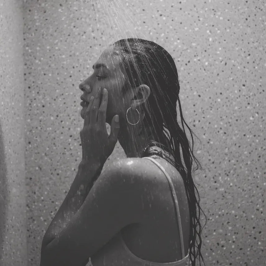 Una mujer duchándose, la pared del baño está revestida por Panel de Pared de Ducha SPC efecto terrazo de revestimientos pared