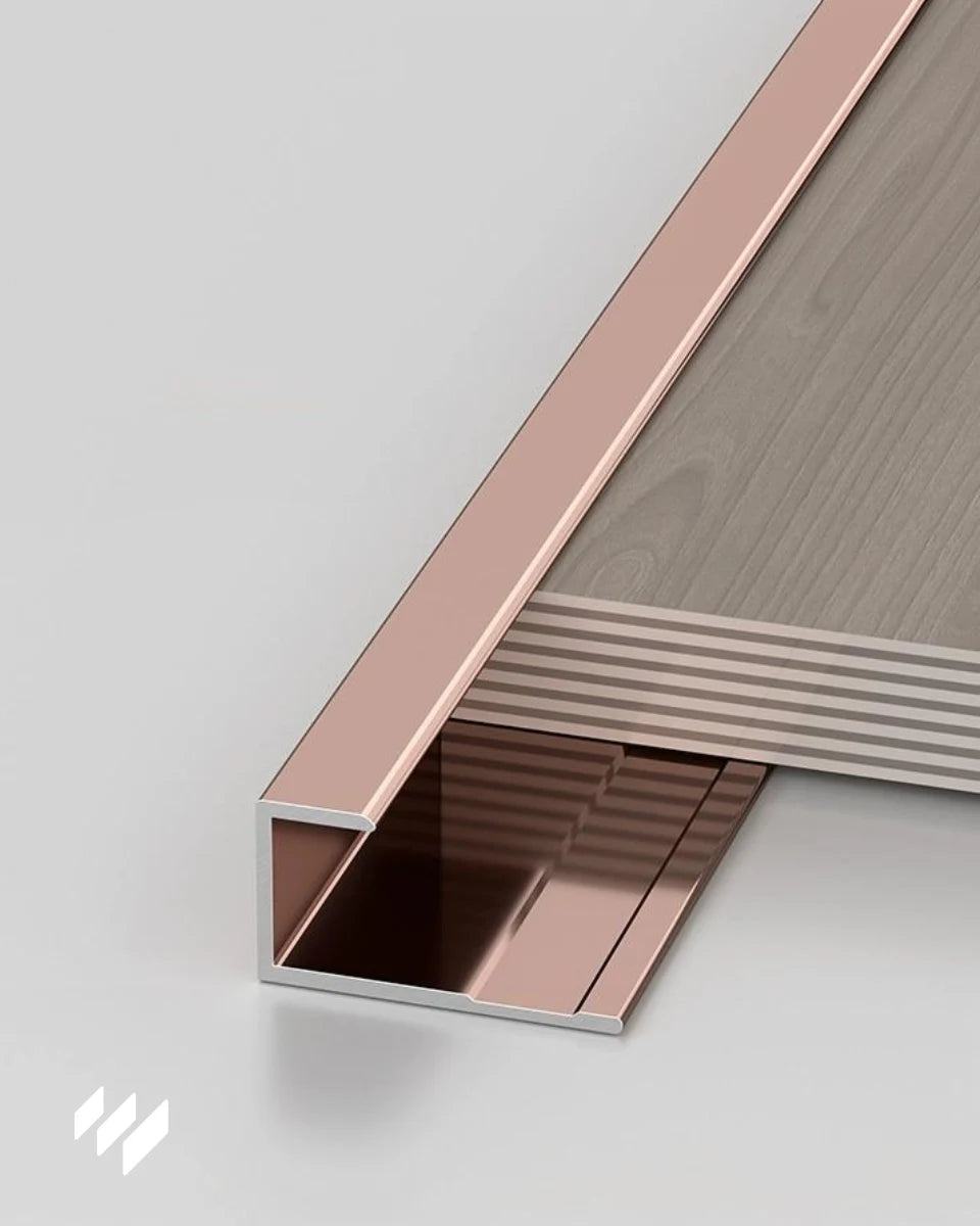Perfil de remate en U de aluminio oro rosa brillante aplicado en el borde de un panel, compatible con sistemas de revestimientos pared