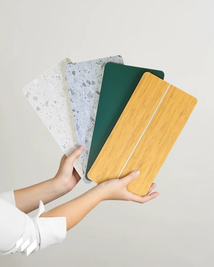 Dos manos presentan en abanico cuatro muestras SPC Versa: terrazo gris claro, terrazo gris, verde liso y efecto madera cerámica.