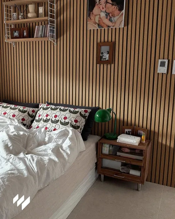 Habitación acogedora con pared decorada en panel acústico de listones en roble natural de revestimientos pared, junto a una cama con cojines estampados y luz cálida.