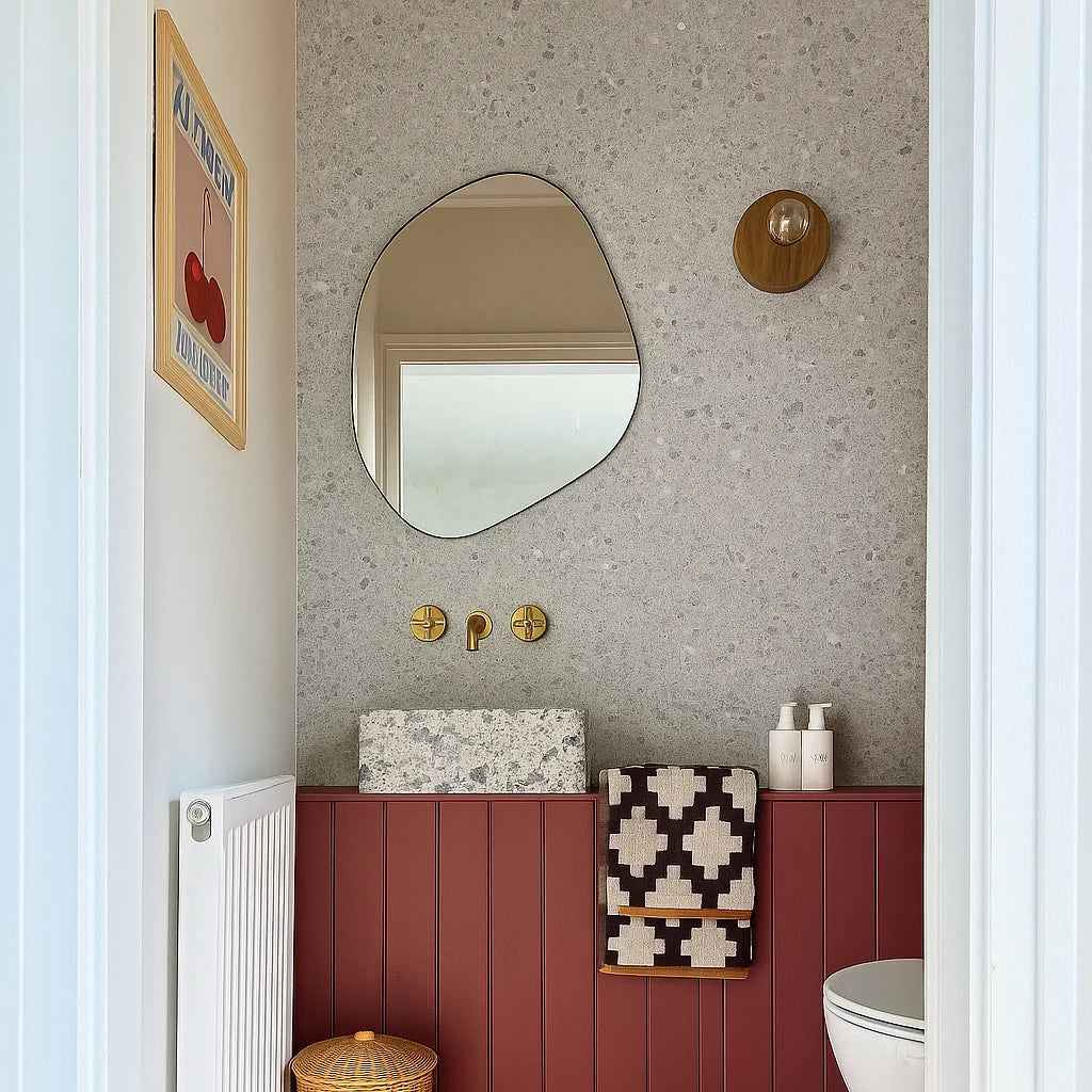 Panel de pared de ducha SPC efecto terrazo aplicado en una pared detrás del lavabo en un aseo moderno y cálido. El acabado de terrazo gris claro contrasta con el zócalo de madera burdeos, reflejando estética responsable, sin químicos y con carácter atemporal.