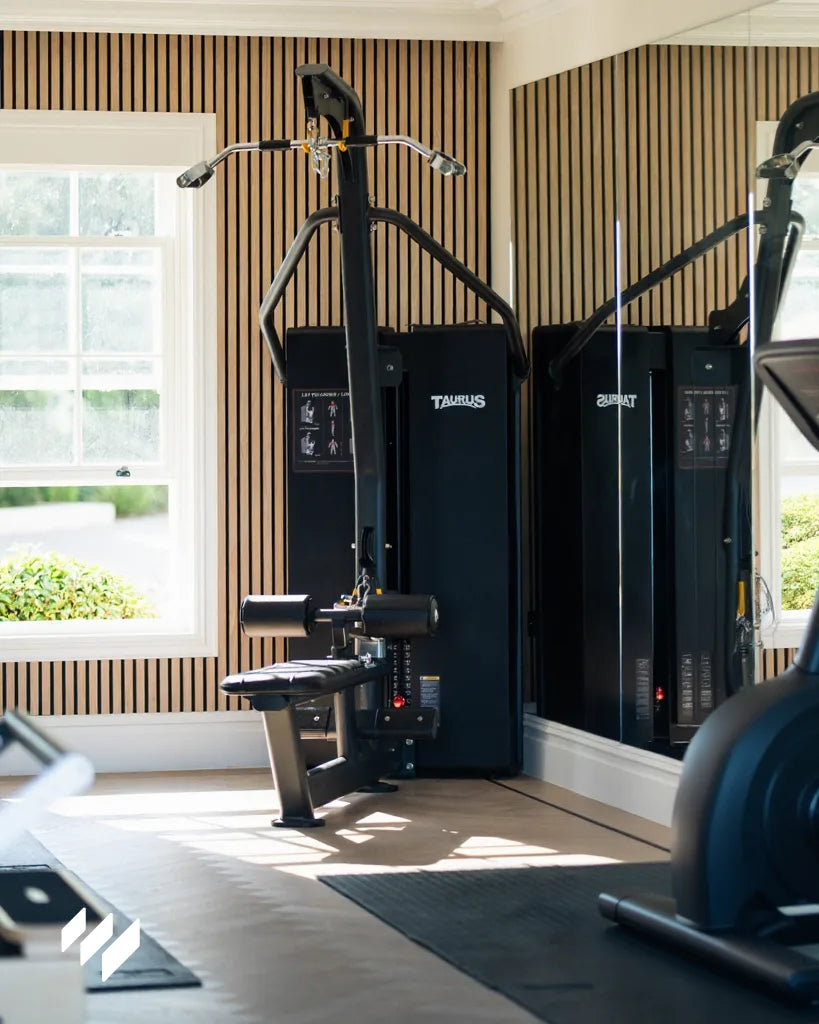 Espacio de entrenamiento doméstico con pared acústica de listones en roble natural de revestimientos pared y maquinaria profesional frente a espejo.