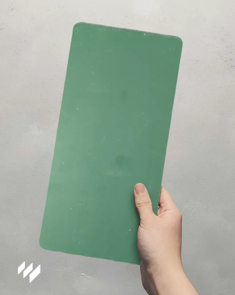 Muestra de Panel SPC imitación azulejo vertical color verde Versa, sostenida con la mano, fondo gris cemento.