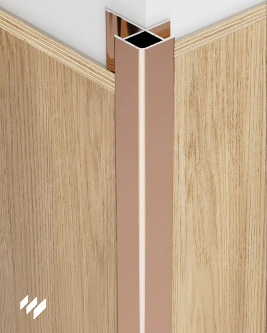 Perfil de Esquina Exterior Cuadrada de Aluminio en color Oro Rosa Brillante instalado en una esquina con paneles decorativos de madera, imagen de revestimientos pared.