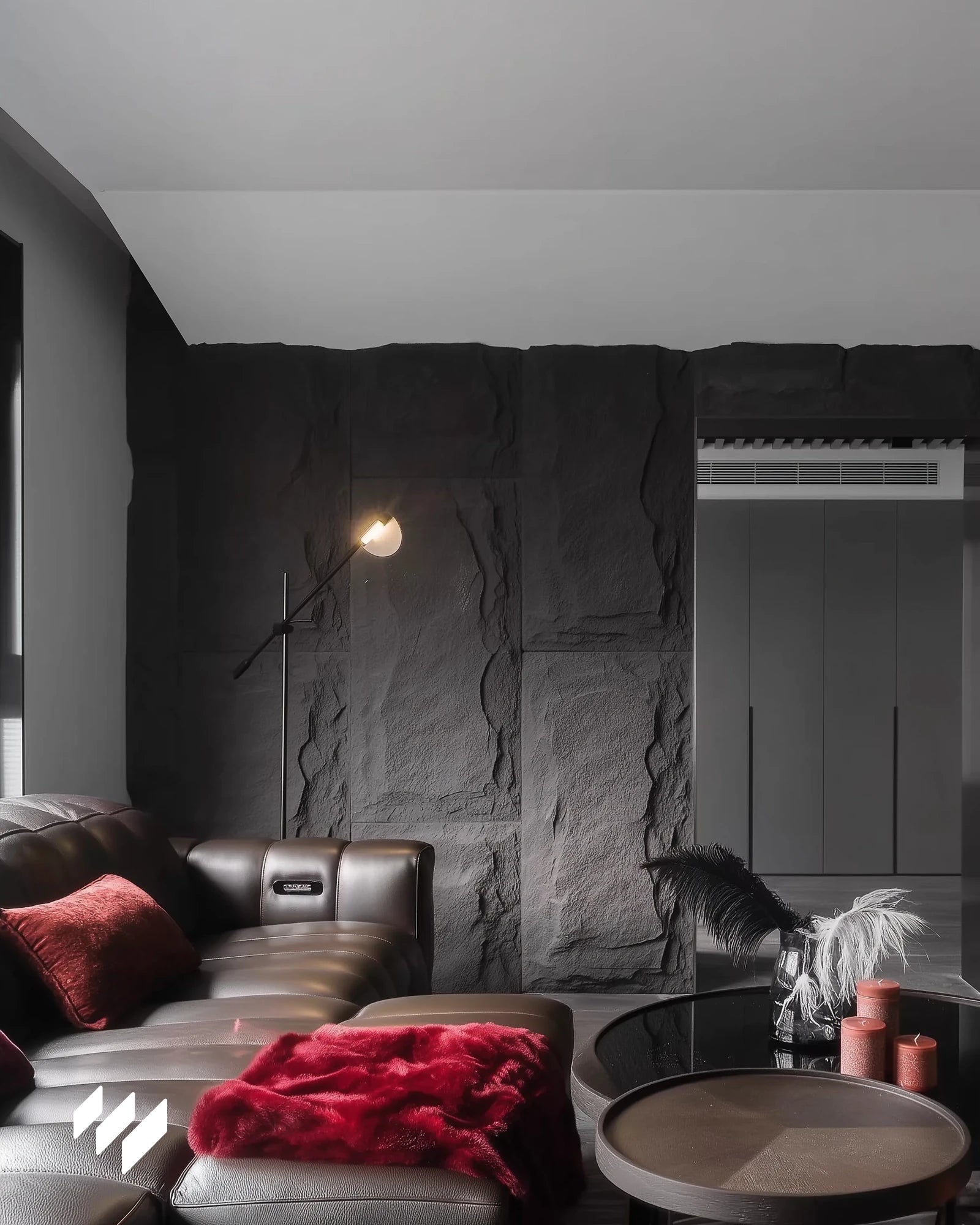 Sala moderna con revestimiento PU efecto piedra Negro Basalto de Revestimientos Pared, acompañada de sofá de cuero marrón y detalles en rojo intenso.