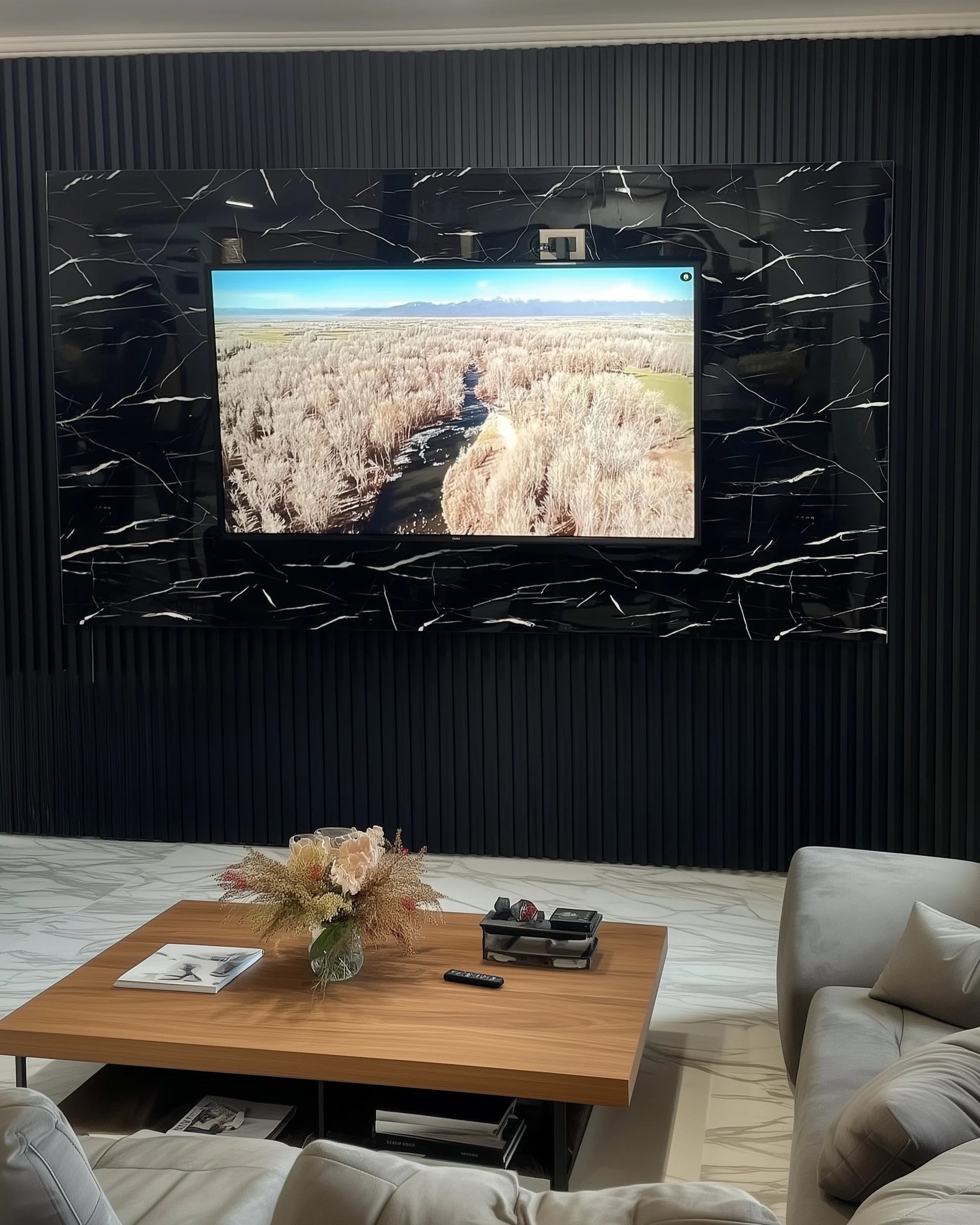 Marta, en su salón de Barcelona, observa un documental de naturaleza en la televisión montada sobre una pared de Panel WPC Alto Brillo efecto Mármol Negro Marquina, con fondo de listones negros y suelo marmoleado.