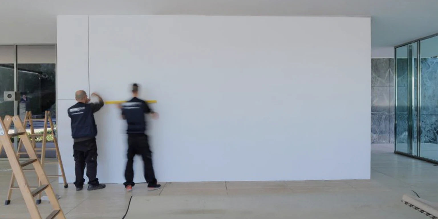 Dos instaladores profesionales midiendo y preparando una pared blanca lisa antes de la instalación de paneles decorativos de alto brillo.