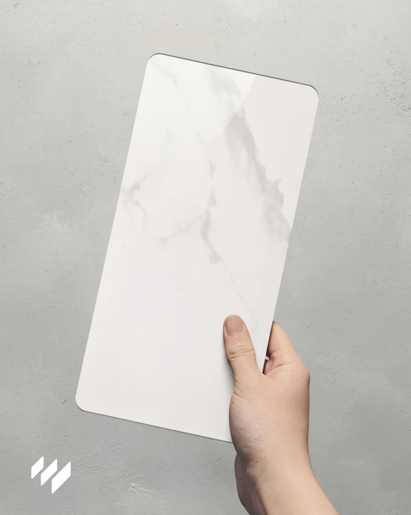 Muestra de panel WPC alto brillo efecto mármol Calacatta Blanco sostenida con una mano, de Revestimientos Pared.