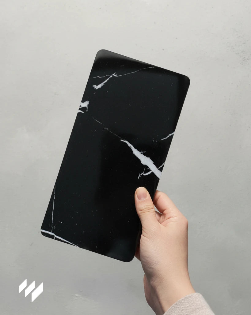 Muestra de panel decorativo WPC alto brillo efecto mármol Negro Marquina sostenida con una mano, de Revestimientos Pared.