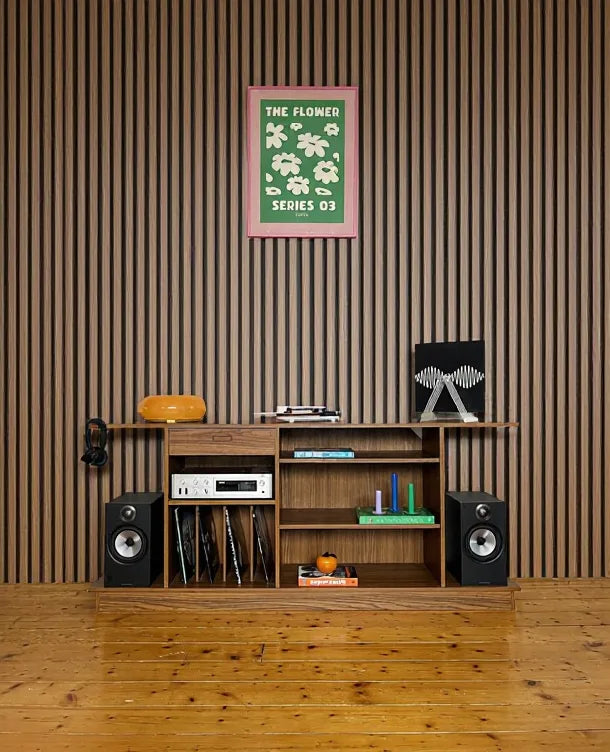 Instalación del Panel Acústico de Listones Nogal Natural de la marca Revestimientos Pared en una pared de salón con mueble de música y altavoces.