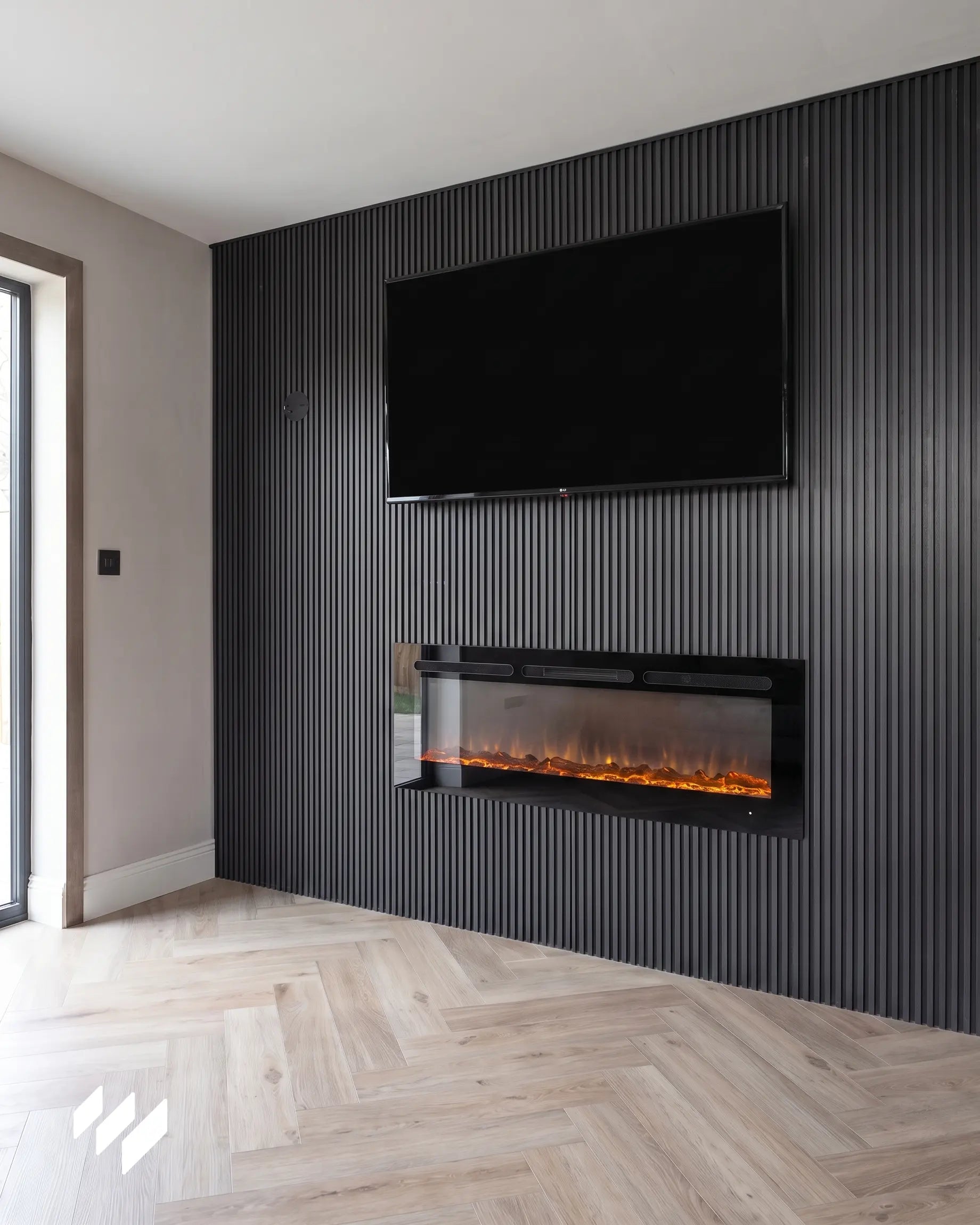 Pared de TV decorada con listones WPC Antracita Metalizado y chimenea eléctrica integrada en un salón contemporáneo de Valencia con suelo en espiga de madera clara.