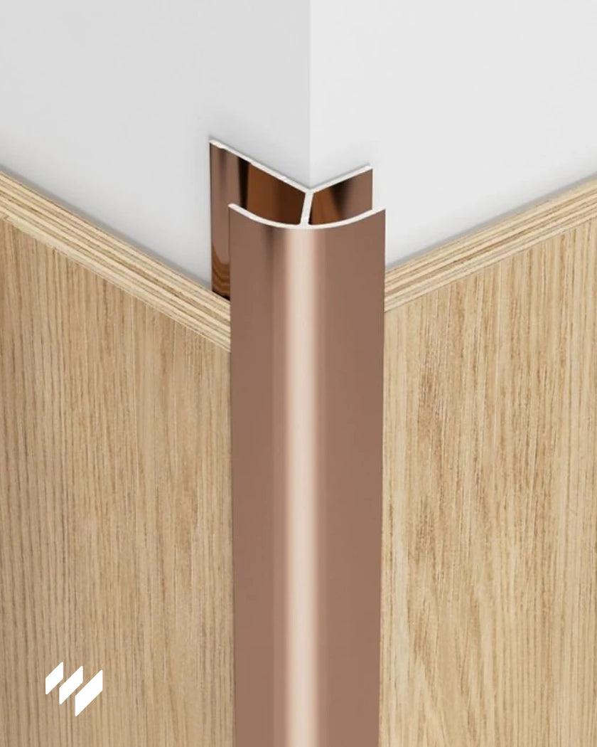 Perfil de esquina exterior redondeada de aluminio en oro rosa brillante instalado en una esquina con paneles efecto madera, de revestimientos pared.