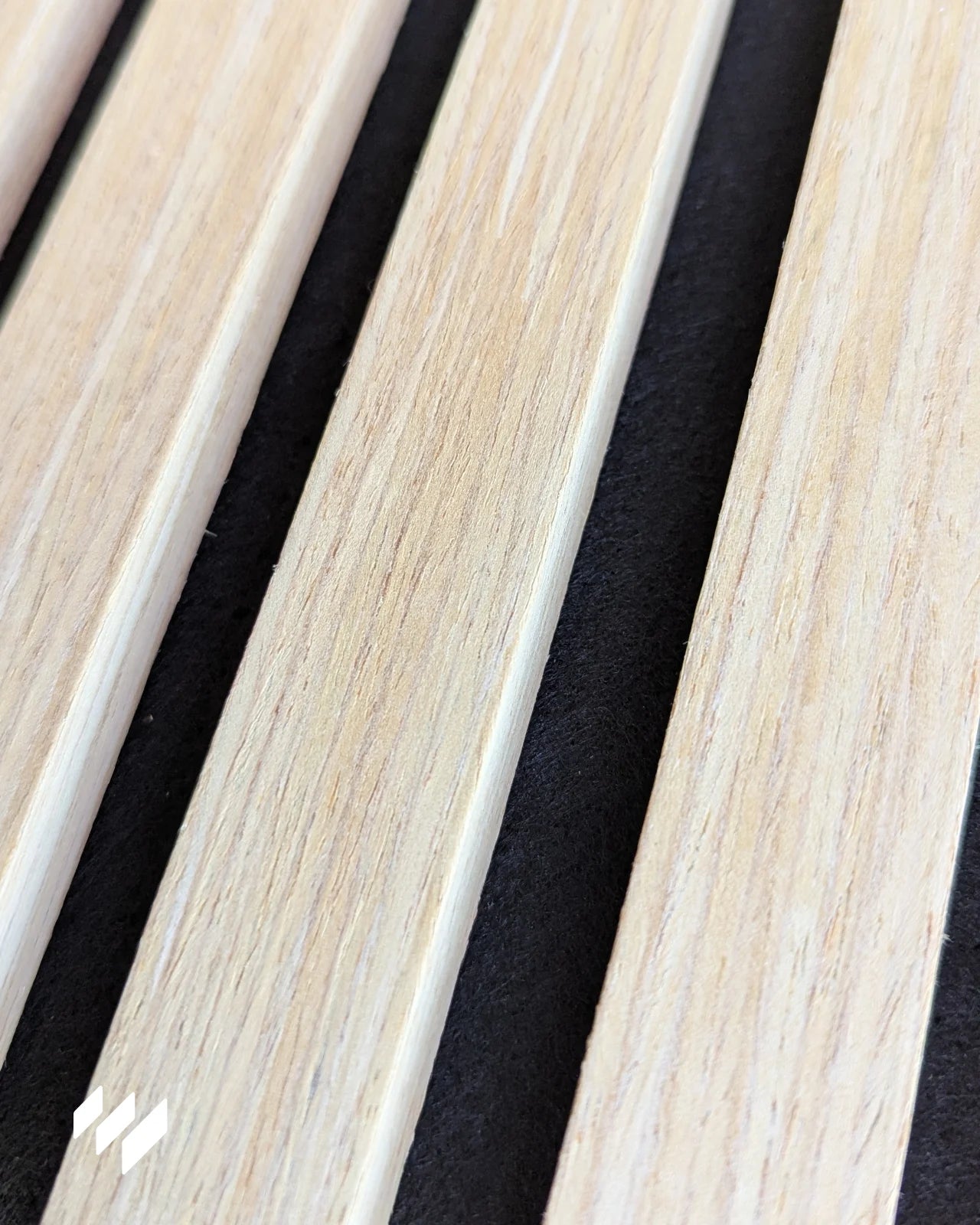 Detalle cercano de la superficie del panel acústico en roble natural, mostrando el acabado de madera y el fieltro PET negro entre listones.