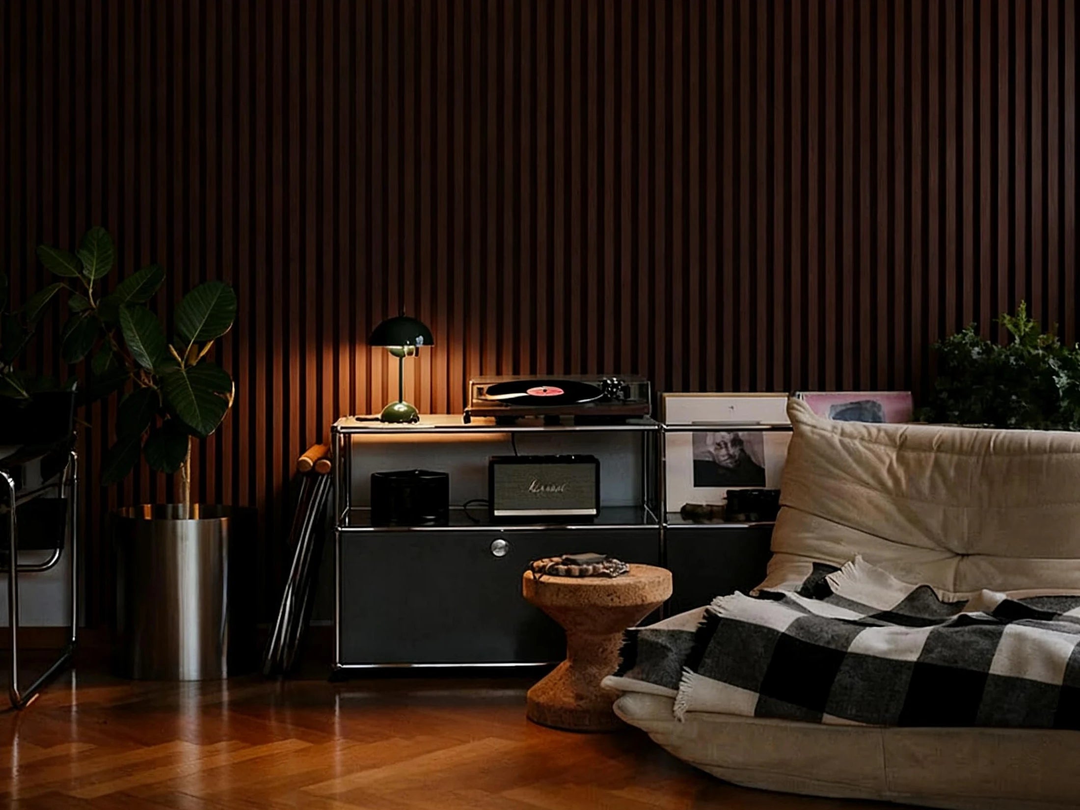 Salón moderno con revestimiento de pared Listones 3D WPC Nogal Oscuro detrás del sofá beige, creando un ambiente cálido y elegante con iluminación ambiental.