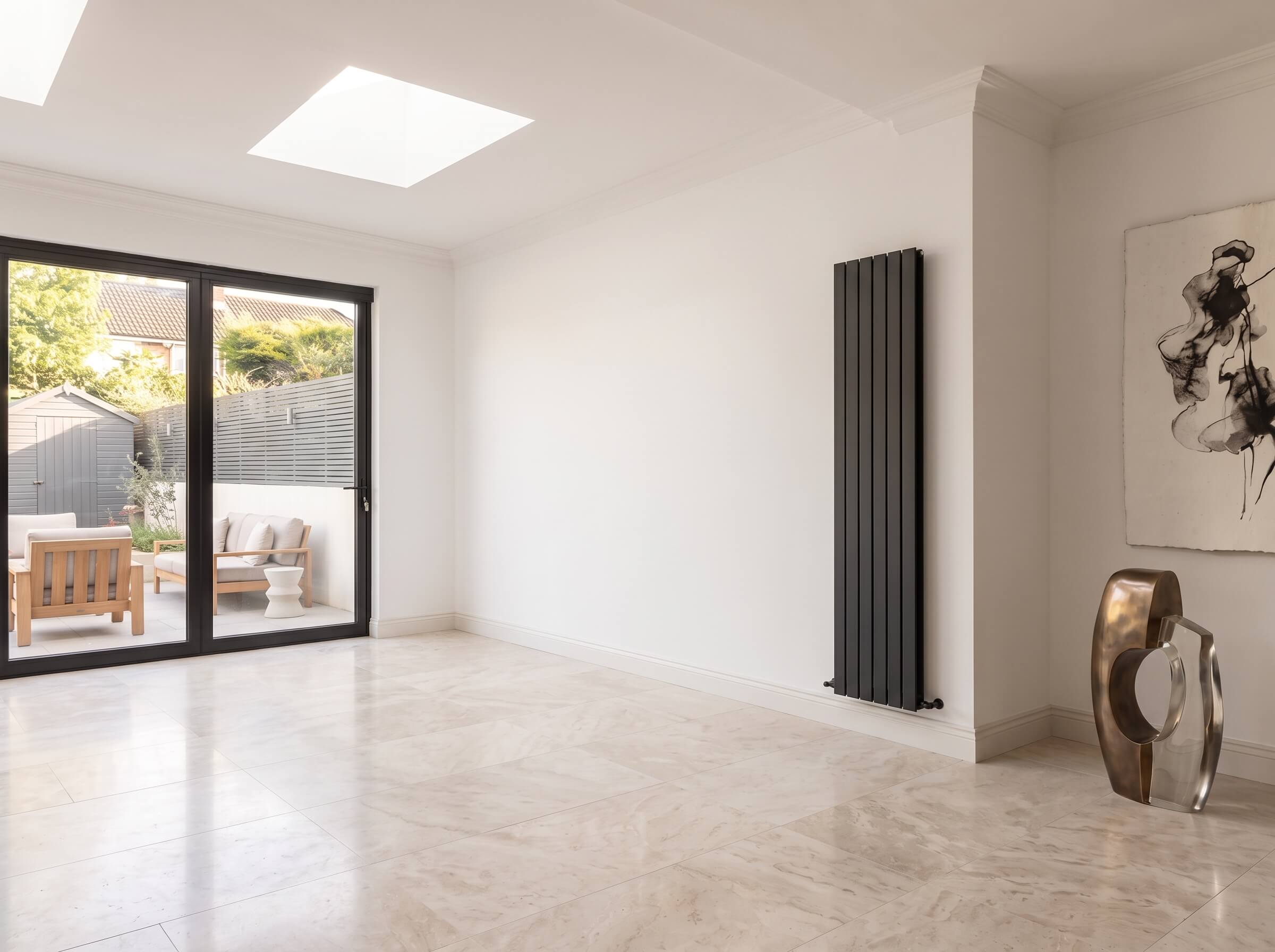 Salón de una villa independiente en Madrid antes de instalar el revestimiento de pared, con pared blanca lisa, radiador vertical negro, suelo de mármol claro y puertas correderas hacia el jardín.