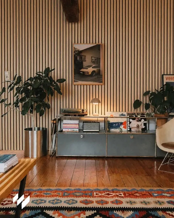 Salón con paneles acústicos de listones en roble natural de revestimientos pared, alfombra de colores vivos y mueble metálico estilo retro.